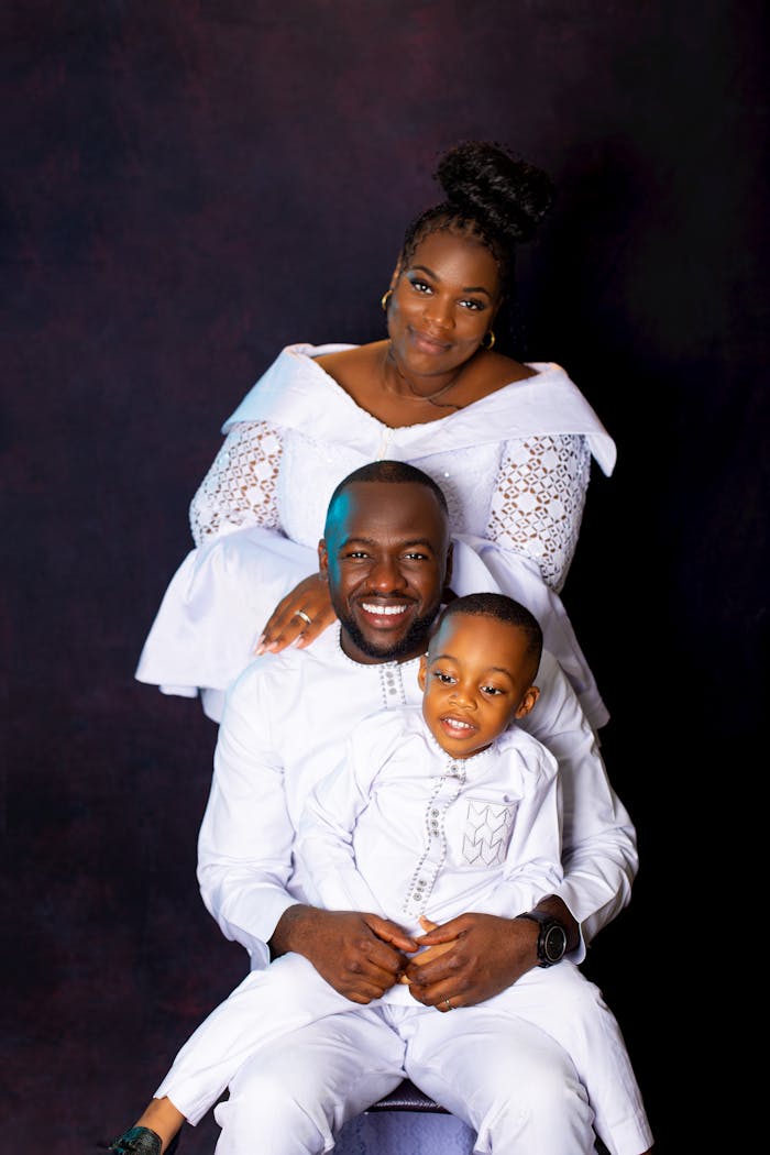 Beautiful family photo with parents and child in white traditional attire on a black background.