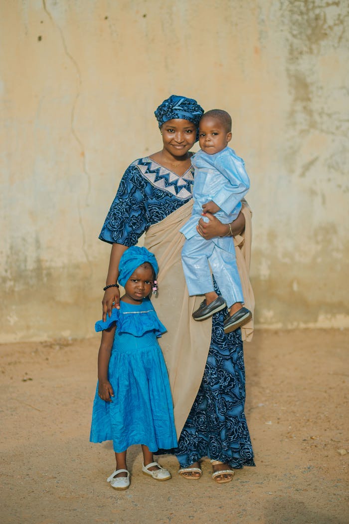 A Nigerian mother with her two children in traditional attire outdoors.