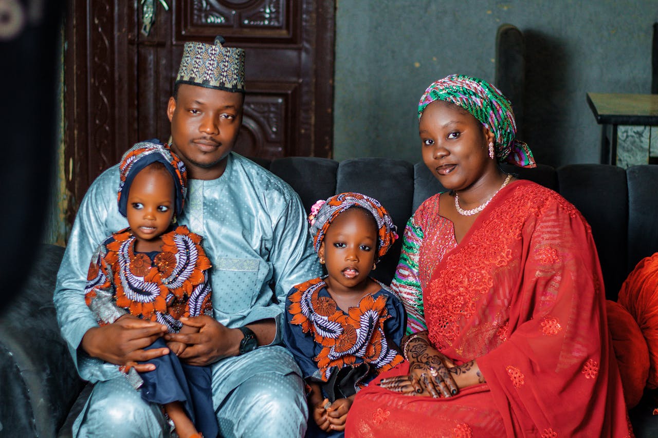 Joyful family portrait featuring parents and two children in vibrant traditional attire, celebrating culture indoors.
